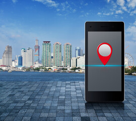 Map pin location button on modern smart mobile phone screen on stone tile floor over city tower,...