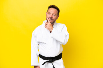 Middle age caucasian man doing karate isolated on yellow background looking up while smiling