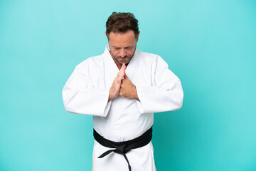 Middle age caucasian man isolated on blue background doing karate and saluting
