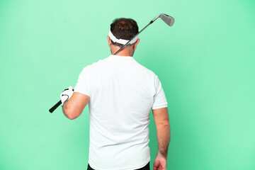 Middle age caucasian man isolated on green background playing golf and in back position