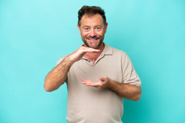 Middle age caucasian man isolated on blue background holding copyspace imaginary on the palm to insert an ad