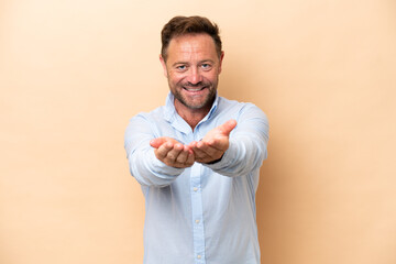Middle age caucasian man isolated on beige background holding copyspace imaginary on the palm to...