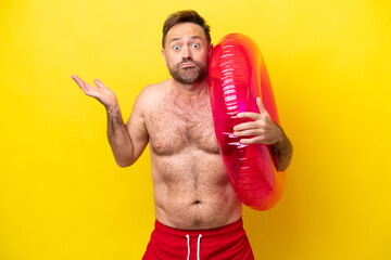 Middle age caucasian man holding inflatable donut isolated on yellow background having doubts while...