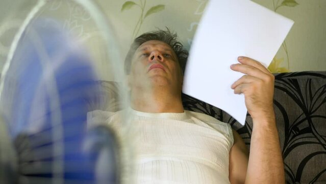 A man cools himself under an electric fan during the summer heat
