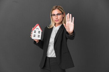 Blonde Uruguayan girl holding a house toy isolated on black background making stop gesture