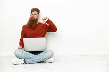 Young reddish caucasian man with laptop isolated on white background showing thumb down with...