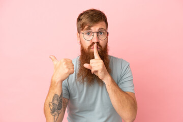 Young reddish caucasian man isolated on pink background pointing to the side and doing silence...