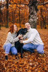Happy young family man and woman have fun walking with their dog in the autumn park, they adore their pet.