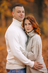 Fototapeta premium A beautiful couple in an autumn park walks and hugs against a background of orange leaves.