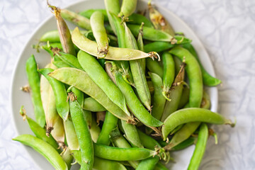 fresh green peas stacked in a bunch on a plate on a light background