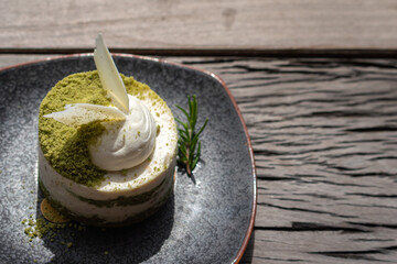 A piece of macha green tea mixed with macadamia cake which is served in black dish, placed on wooden table. Food close-up photo, selective focus.