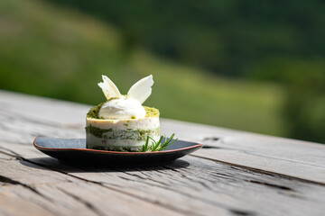 A piece of macha green tea mixed with macadamia cake which is served in black dish, placed on...