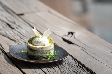A piece of macha green tea mixed with macadamia cake which is served in black dish, placed on wooden table. Food close-up photo, selective focus. - obrazy, fototapety, plakaty