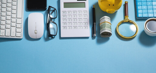 Piggy bank, money, coffee, calculator, eyeglasses on the blue background.