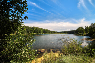 Beautiful lakeside view from a small lake in Russia, with lush green trees, blue sky and sunlight