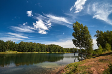 Beautiful lakeside view from a small lake in Russia, with lush green trees, blue sky and sunlight