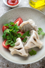 Close-up of georgian meat dumplings khinkali with fresh parsley and tomatoes in a beige plate, vertical shot, selective focus