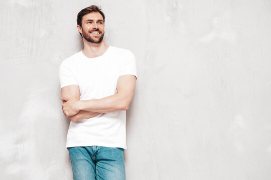 Portrait of handsome smiling stylish hipster lambersexual model. Sexy man dressed in T-shirt and jeans. Fashion male isolated on grey wall in studio. crossed arms
