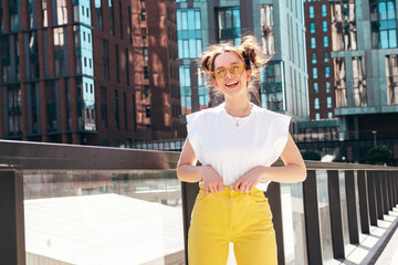 Young beautiful smiling hipster woman in trendy summer yellow jeans clothes. Carefree teen model posing in the street at sunset. Positive female outdoors