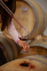 winemaker woman takes a sample of wine from a barrel and pours a little into a glass with special tool