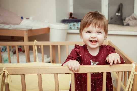laughing happy babu girl stands in a crib in a children's room