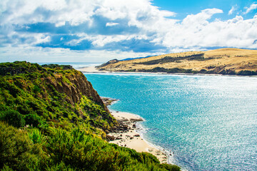 Fototapeta na wymiar Rocky cliff and narrow sandy beach beneath it at the neck of Hokianga Harbour. Signal Station Track, Arai te Uru, Northland, New Zealand