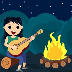 cute little girl sits and plays the guitar by the fire at night.