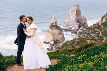 Fototapeta na wymiar the groom hugs and kisses the bride on ocean coast overlooking t
