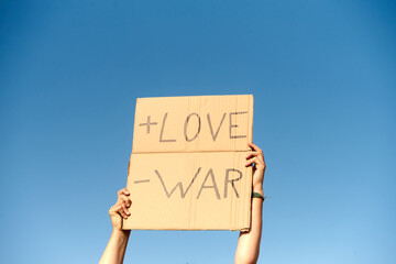 A Cardboard Signs saying More Love, Less War. Held by two hands on sky background
