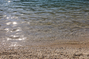 Small pebble stones on sea beach with transparent water. Background for summer vacation