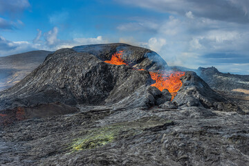 Active volcano on Iceland's Reykjanes Peninsula. Landscape in spring with sunshine. Liquid lava flows out of the side of the crater. little steam rises. Clouds in the sky