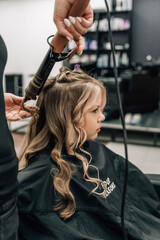 Fototapeta premium Female hands of a hairdresser. Close-up of blond hair on a curling iron. Curling curls. Beauty saloon.