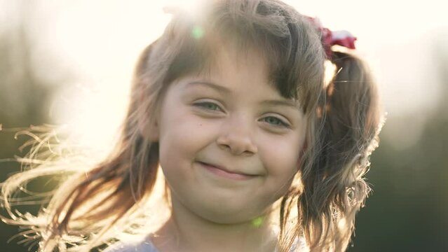 Happy girl in the sun in wind. Close-up of the girl face in the park. Dream girl. Hair in the wind. The child smiles at the camera. Girl's dream. Face close-up. Happy child in the park. Beautiful face