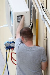 European serviceman repairs air conditioner outdoor wall unit. AC filling with pressure manometers...