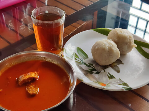 A glass of black tea (Sulaimani) with Delicious Kerala style breakfast dishes  white snacks(Kozhukatta) and fish curry served on a table
