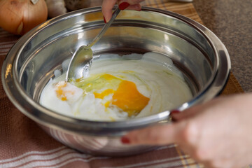 Female hands stir fresh eggs from bowl..