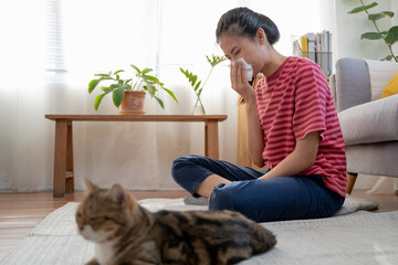 Diseases from pets concept. Woman is sneezing from fur allergy on the sofa and playing with her cat.