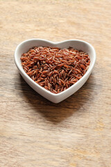 red long grains rice in heart shaped plate on wooden background close up