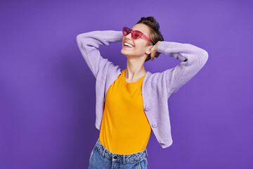 Relaxed young woman holding hand behind head while standing against purple background