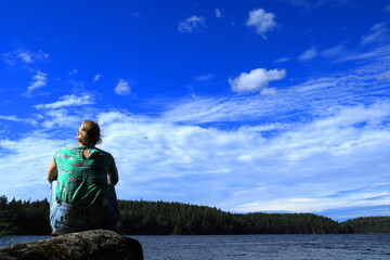 Fototapeta premium Scandinavian summer weather one sunny day. Woman sitting on a rock with back to camera. Next to the Swedish lake Malar or Mälaren. Great view. Järfälla, Stockholm, Sweden, Scandinavia, Europe.