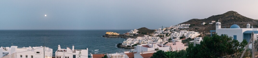Panoramic view of a coastal town of white houses on the Mediterranean coast with a full moon over the sea after sunset