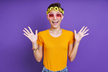 Excited funky woman with floral head wreath gesturing while standing against purple background