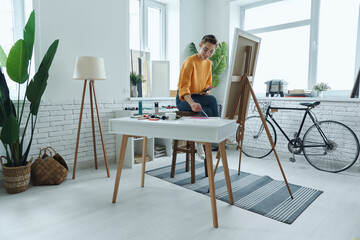 Beautiful young woman mixing colors while drawing in art studio