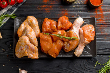 raw marinated chicken for barbecue, chicken fillet, chicken wings, chicken legs on dark plate on black wooden table top view