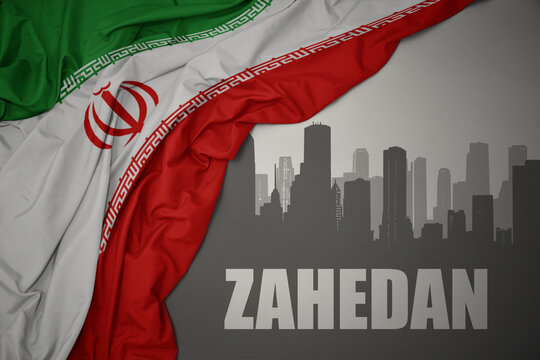 abstract silhouette of the city with text Zahedan near waving national flag of iran on a gray background.3D illustration