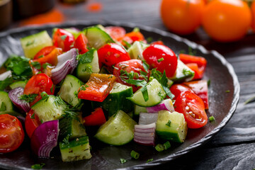 Vegetable salad with tomatoes and cucumbers on black plate on dark table macro close up