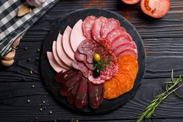 slicing of different meat on black stone plate top view on dark wooden table