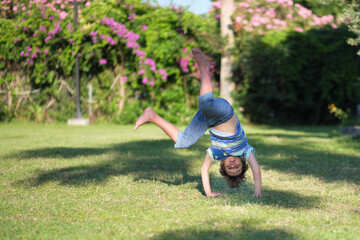 Fototapeta na wymiar Mischievous preschooler boy somersaults on sand grass in the park.