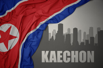 abstract silhouette of the city with text Kaechon near waving national flag of north korea on a gray background.3D illustration
