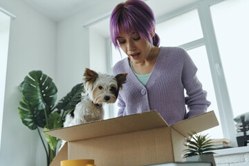 Surprised young woman and little cute dog looking inside a box
